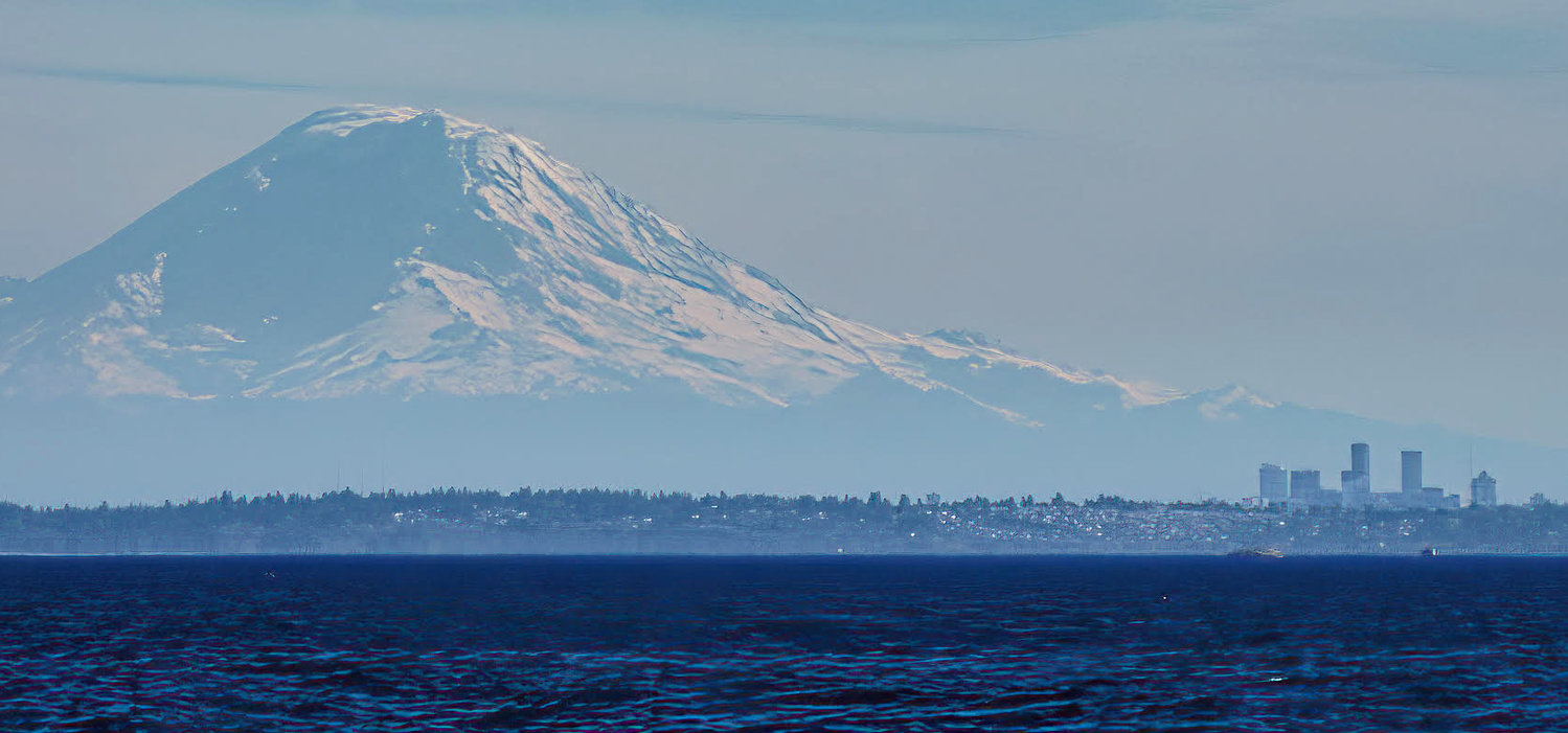 The view of Mount Rainier, looking south from Point No Point beach, with the skyline of Seattle in the right foreground.